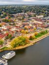 Aerial view of Stillwater, Oklahoma, highlighting the scenic downtown area near the waterfront, lush greenery, historic buildings, and boats docked along the river, perfect for tourists exploring Payne County.